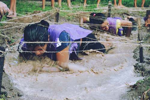 muddy water two women crawling on mud with rope wet